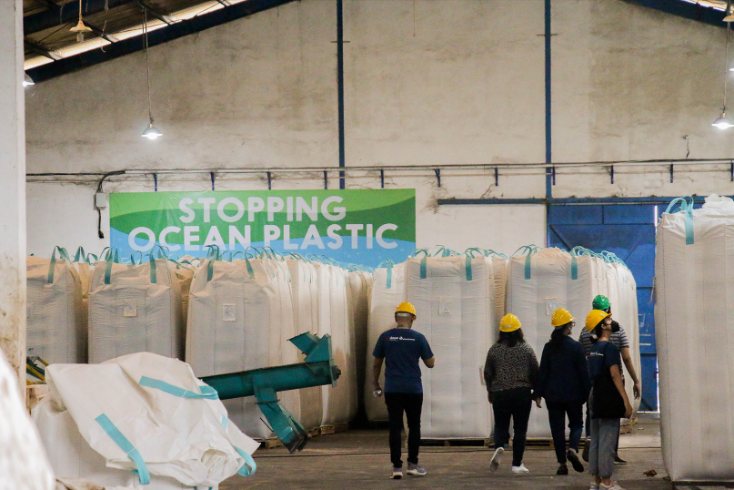 Group walking past bales of collected plastic