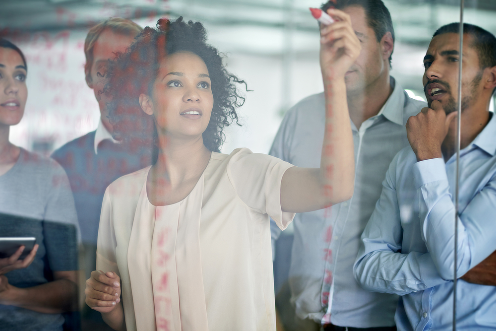 A group of employees brainstorming on a transparent whiteboard.