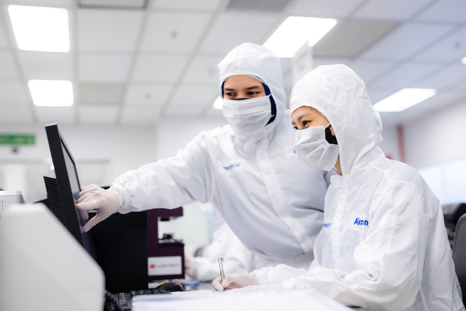 Lab employees in protective clothing, looking at computer screen