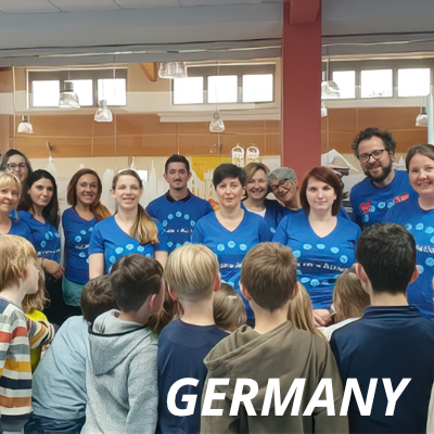 A group Alcon volunteers in blue t-shirts speaking with schoolchildren in Germany