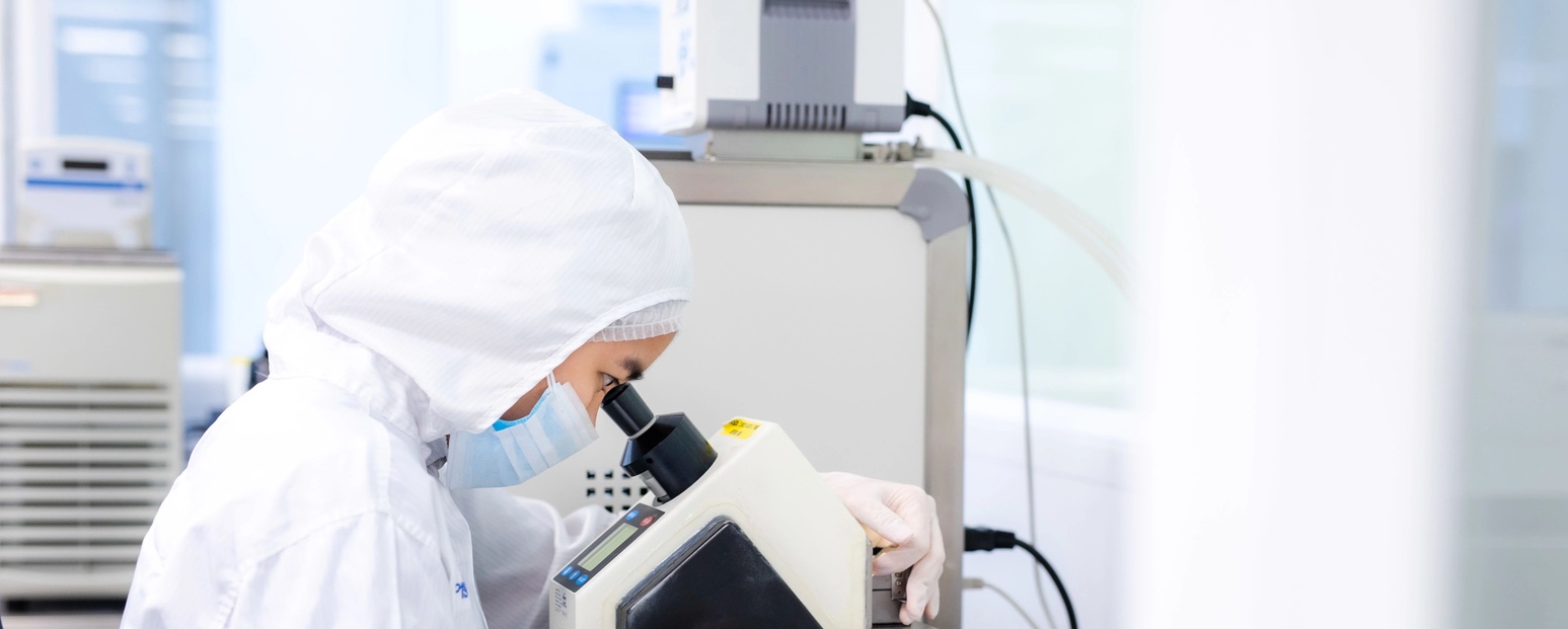 Woman in lab gear looking into microscope