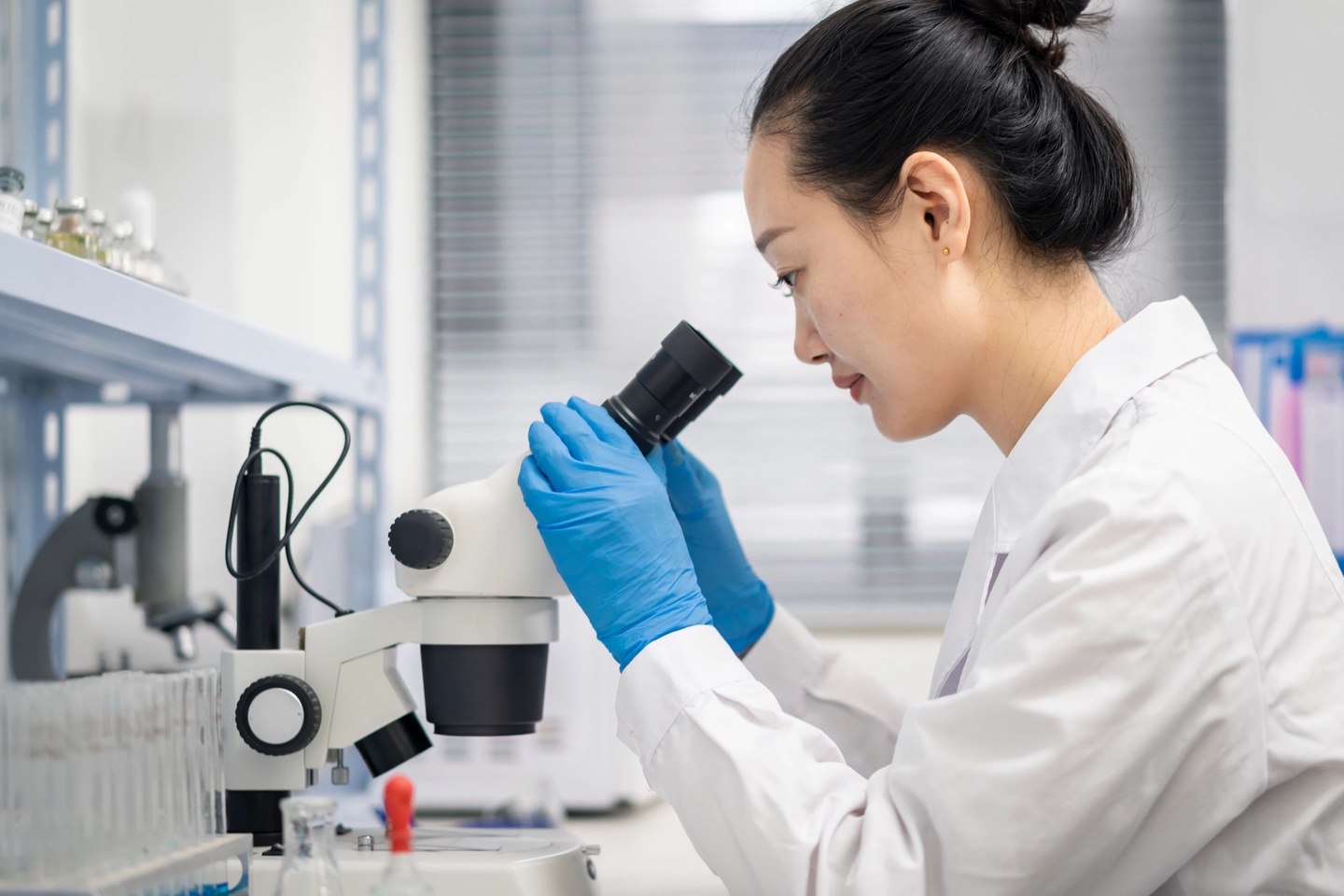 Woman in lab gear looking into microscope